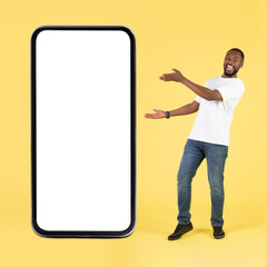 Joyful Black Guy Showing Large Phone Screen Over Yellow Background