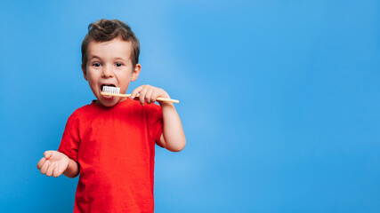 Smiling boy with healthy teeth brushing his teeth with a toothbrush on a blue isolated background....
