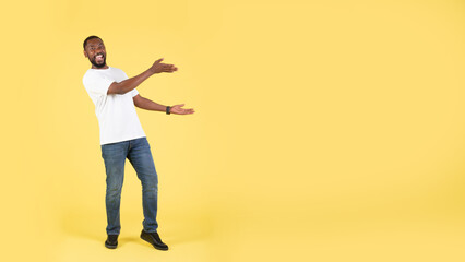 Fototapeta na wymiar African Male Showing Blank Space With Both Hands, Yellow Background