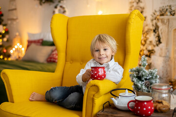 Cute child, boy, sitting on a yellow armchair in a decorated room for Christmas
