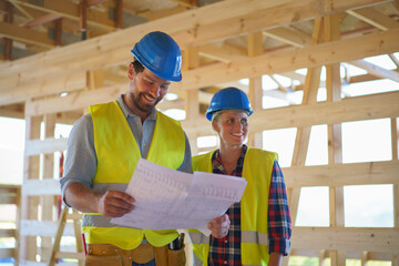 Construction engineers or architects with blueprints checking eco building site of wood frame house