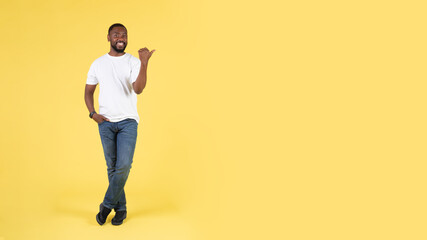 Cheerful African American Guy Pointing Thumb Finger Aside, Yellow Background