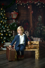 Cute child, holding suitcase and teddy bear, waiting at home for holidays