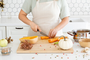 A woman cutting a carrot to prepare a tasty pumpkin soup for family. Meal preparation. Food picture. Holidays and cosy evening with family