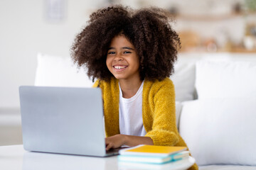 Positive african american child studying from home, using laptop