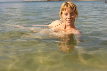 Beautiful woman swimming in the ocean. Smiling blonde girl enjoy in sunny day..
