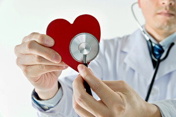 Male doctor with stethoscope examining red heart against white background