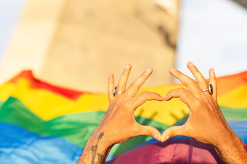 Hands making heart sign in front of rainbow flag..