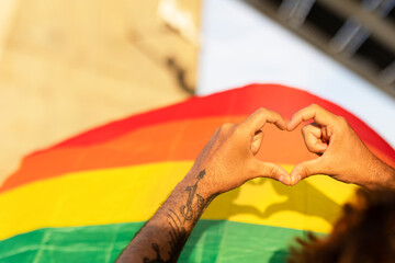 Hands making heart sign in front of rainbow flag..