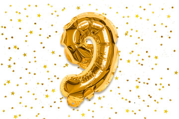 The number of the balloon made of golden foil, the number nine on a white background with sequins....