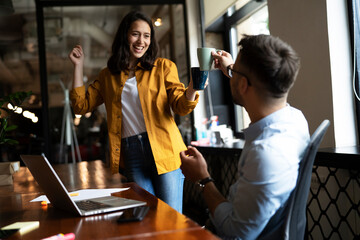 Colleagues laughing in office. Businesswoman and businessman drinking coffee..