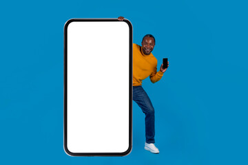 Funny african american man standing behind big smartphone, mockup
