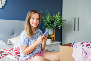Smiling woman using smartphone to find places where to donate or sale clothes. Decluttering,...