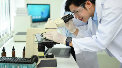 Professional biotechnology specialist looking under microscope, conducting experiment in a laboratory