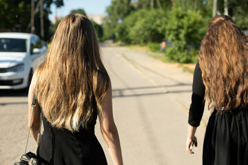 Two girls in black dresses walk down road. Girls return from funeral. Black clothes.