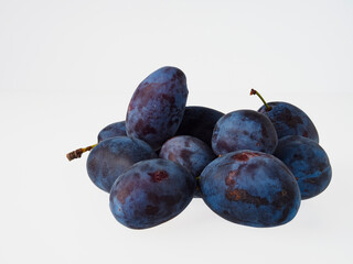 Black plums on wood background. Pile of black plums on a white serving plate. close up