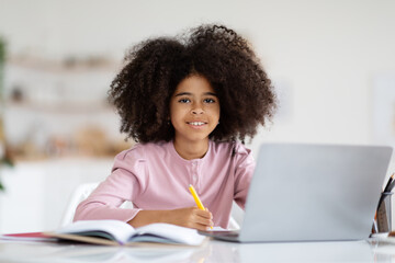 Pretty black little girl doing homework, using computer
