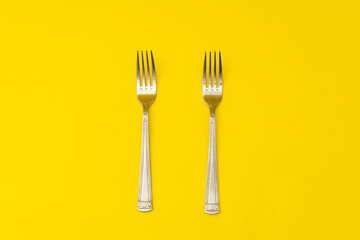 Silver forks lie on a yellow background, minimalism