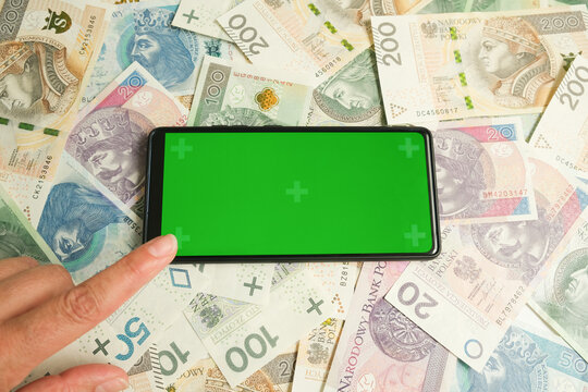 Green screen against the background of paper money. The person's index finger points to the green screen of the gadget. A place for your text on a financial topic. High quality photo