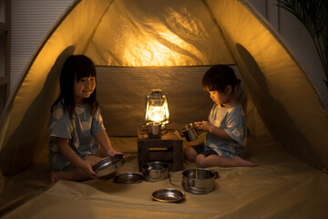 自宅の部屋でテントを張ってキャンプ遊びをしている2人の女の子の姉妹 © kai