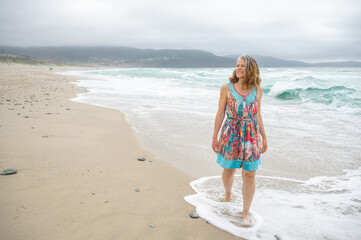 Fototapeta na wymiar An adult woman walks along an empty and wild beach with waves from the sea.
