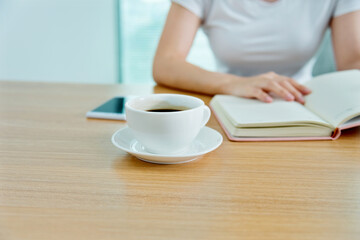 Woman reading book with cup of coffee on table