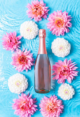 Pink sparkling wine surrounded by pink and white dahlias in water, top view
