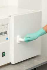 Beautician in protective gloves close the door of the machine for disinfection of tools before the...