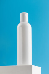  An empty bottle with a cosmetic product on a pedestal on a blue background. Micellar water, facial cleansing lotion.