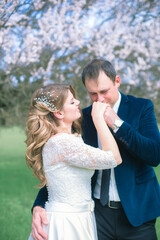 The bride and groom with blond long hair in a white dress in a spring garden near a flowering tree. Emotions and feelings