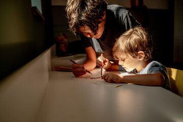 Two brothers draw with colored pencils, the older brother teaches the younger one to draw, the...