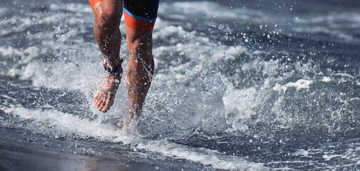 Triathlete swimmer running out of ocean finishing swim race. Fit man ending swimming sprinting...