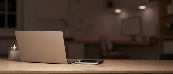 Modern office workspace at night close-up, laptop and copy space over blurred office background.