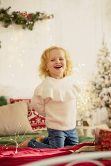 Cute little toddler curly girl in winter christmas sweater, sitting in cozy room, decorated for christmas