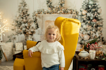Cute little toddler curly girl in winter christmas sweater, sitting in cozy room, decorated for...