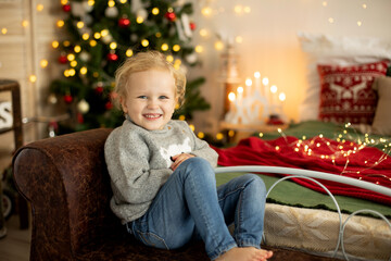 Cute little toddler curly girl in winter christmas sweater, sitting in cozy room, decorated for...