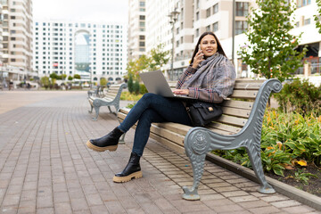 young woman working on a laptop online in the park on a bench, freelance work concept