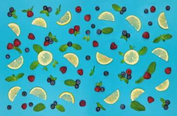 pattern from fresh  blueberries , raspberries , lemon in slices and green mint leaves on bright blue background. Top view, flat lay.