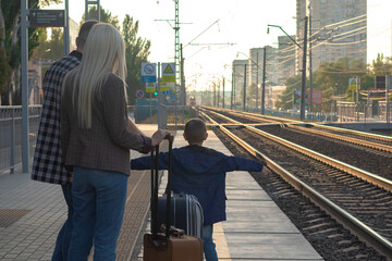 a family of three waiting on an empty railway platform for the arrival of a train
