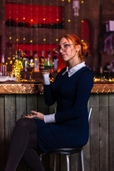 A red-haired girl is sitting in a bar with a book in her hands