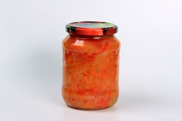 Preparation of canned lecho, canned sweet bell peppers in a glass jar on a white background. Homemade letcho with paprika, tomatoes and carrots