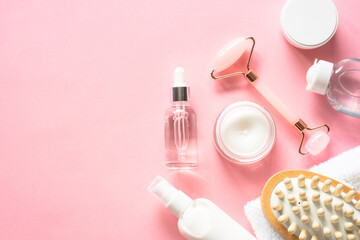 Fototapeta na wymiar Natural cosmetics on pink. Skin care product, cream, soap serum, jade roller and white towel. Flat lay image with copy space.