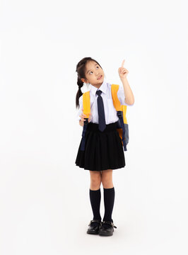 Back to school concept. Cute asian junior school student kid in uniform with yellow backpack posing finger pointing on white background.