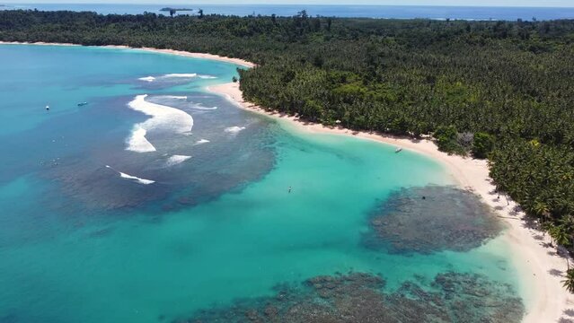 Aerial drone shot of beautiful clear rocky reef sandy beach bay Beng Bengs holiday destination travel tourism palm trees waves boats Mentawai Islands Indonesia Sumatra Asia 4K