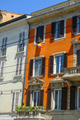Fototapeta na wymiar facade of an orange house in the old town of Parma, Italy with Rainbow banners, and flags. LGBTQ+ banner