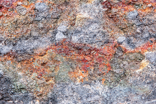 Rough relief surface of natural stone interspersed with rusty orange, red, light green, gray and yellow colors