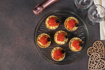 Festive tartlets with red caviar, egg and melted cheese, decorated with black olives on round plate, Top view