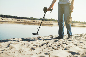 Man with metal detector walks along the sandy river bank. Search for treasures and metal for recycling