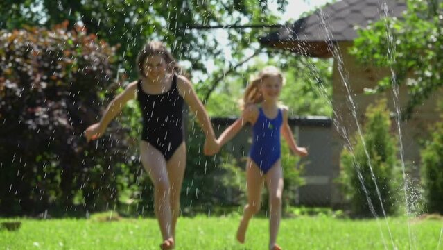Cute girls are running in the water jets from a revolving water sprinkler