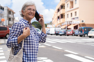 Seniorwoman crossing the street talking on cell phone - elderly lady in an urban street holding...